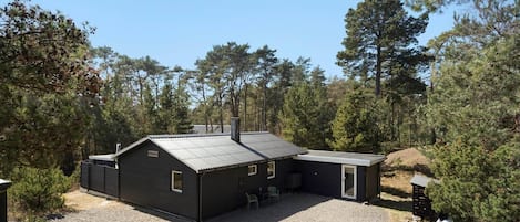 A two-story cabin with a gravel driveway and a small patio area.