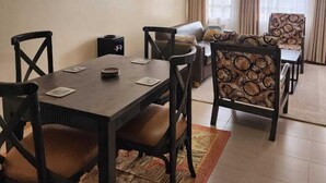 A dining area with a wooden table and chairs, a sofa, and a patterned rug. - Lux Suites Ole Nairi Holiday Homes (Ngong)