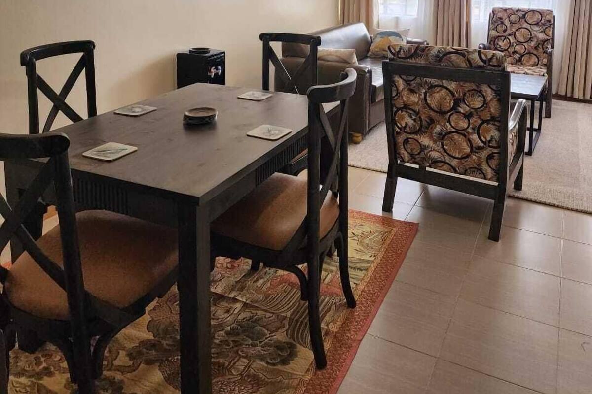 Zona pranzo con tavolo e sedie in legno, un divano e un tappeto decorato.