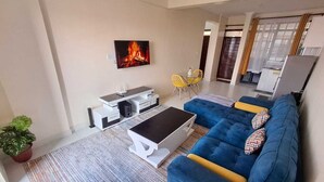 A living room with a blue sofa, a white coffee table, a TV, and a fireplace. - Lux Suites Ole Nairi Holiday Homes (Ngong)