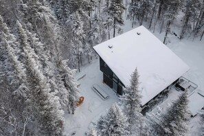 Un chalet moderne, recouvert de neige, entouré d’une forêt dense.