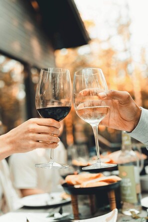 Deux personnes, chacune tenant un verre de vin, l’une un verre de vin rouge et l’autre un verre de vin blanc, sont assises à une table où se trouvent de la nourriture et une bouteille en arrière-plan.