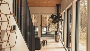 Un interior moderno con techo de madera, una escalera y grandes ventanales con vistas al exterior.