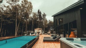 Een houten terras met een zwembad en een jacuzzi, omgeven door hoge bomen en moderne architectuur.