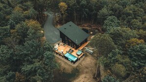 Luchtbeeld van een chalet, omringd door dicht bos, met een zwembad, terras en een hottub.