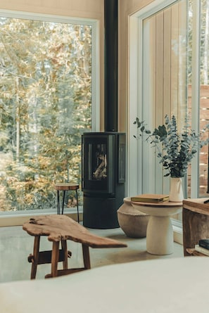 Una habitación acogedora con un ventanal grande, una chimenea, un banco de madera y una planta en maceta.