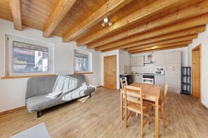 Une pièce avec un plafond en bois, un canapé, une table à manger avec des chaises et un coin cuisine.