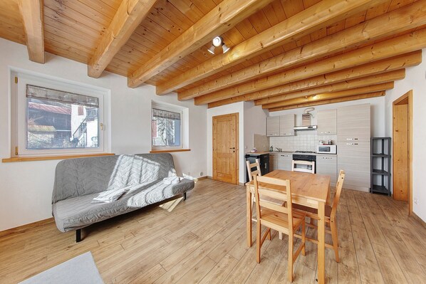 A room with a wooden ceiling, a sofa, a dining table with chairs, and a kitchen area.