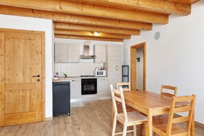 A kitchen with wooden cabinets, a black refrigerator, a wooden dining table, and chairs.