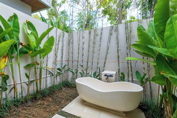 A modern outdoor bathroom with a freestanding bathtub, surrounded by lush greenery and a bamboo fence. - Villa Linaria by Pertama Stay (Ungasan)
