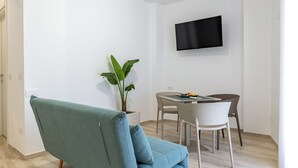 Una sala de estar moderna con un sofá color turquesa, una mesa de comedor con sillas, una planta en maceta y un televisor montado.