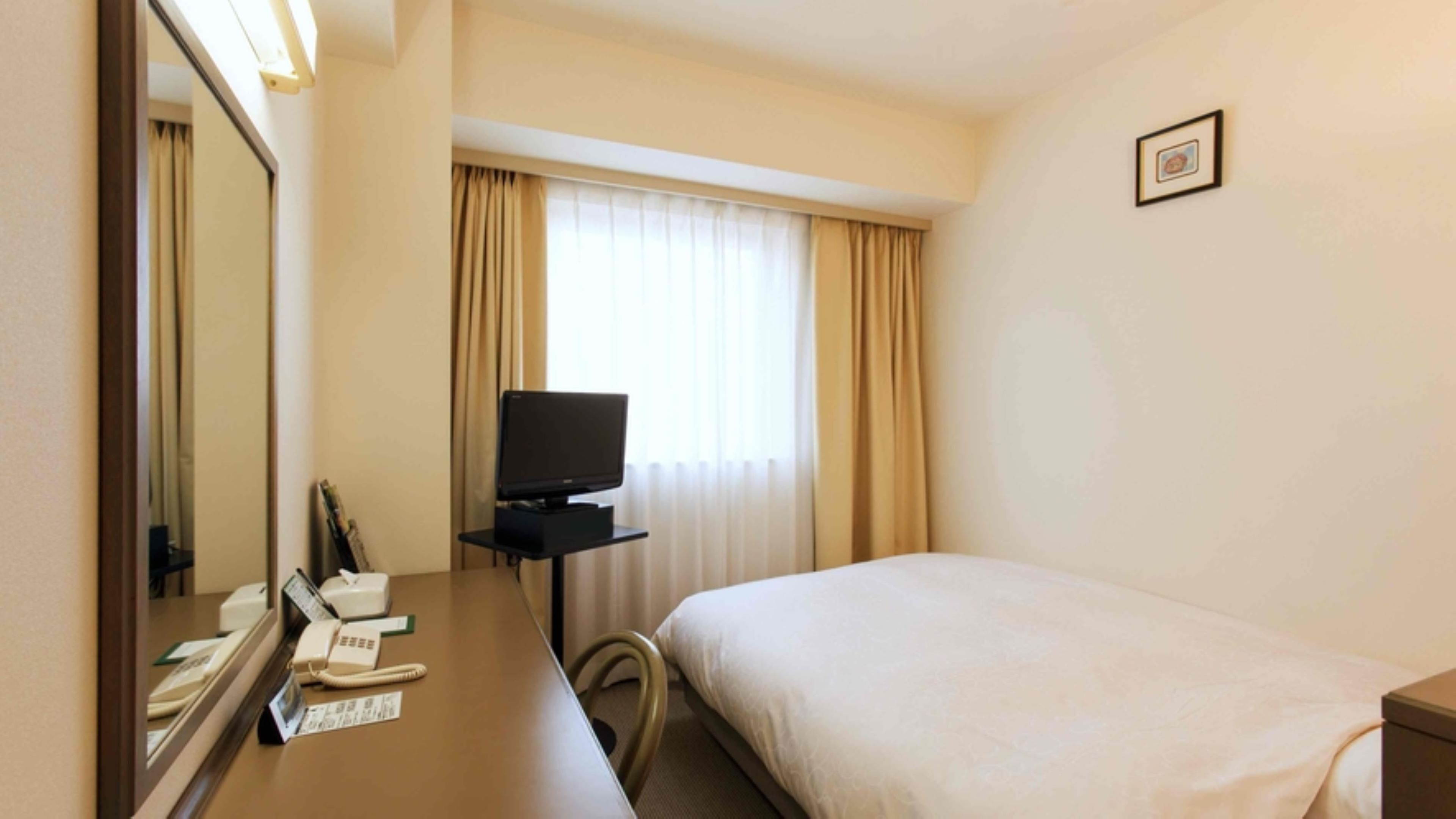 Ein Hotelzimmer mit Bett, Schreibtisch mit Telefon, Fernseher und einem Fenster mit Vorhängen.