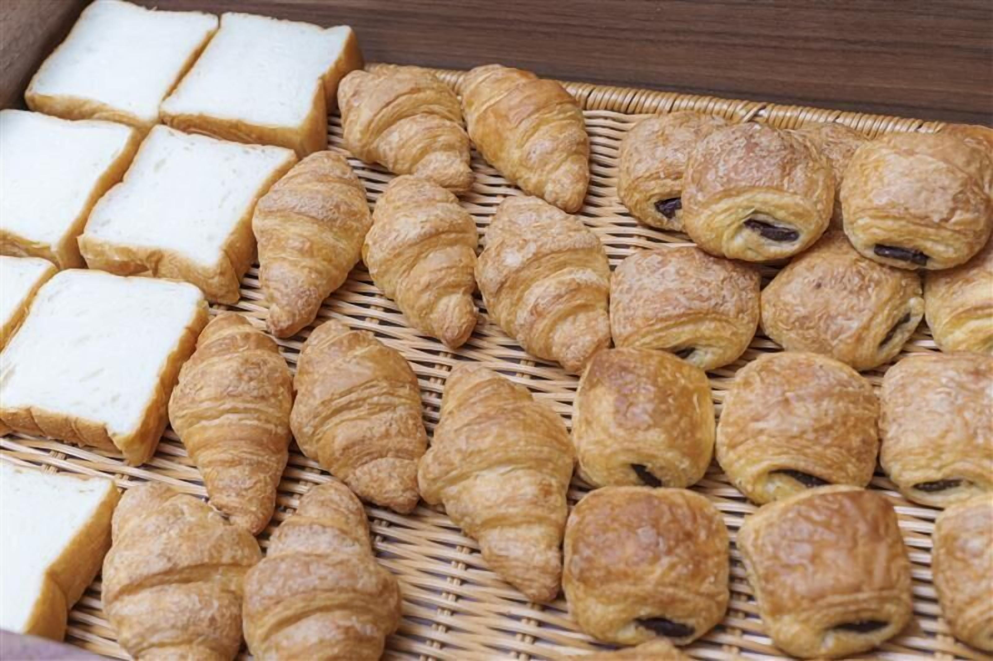 A variety of pastries including croissants and bread on a woven surface.