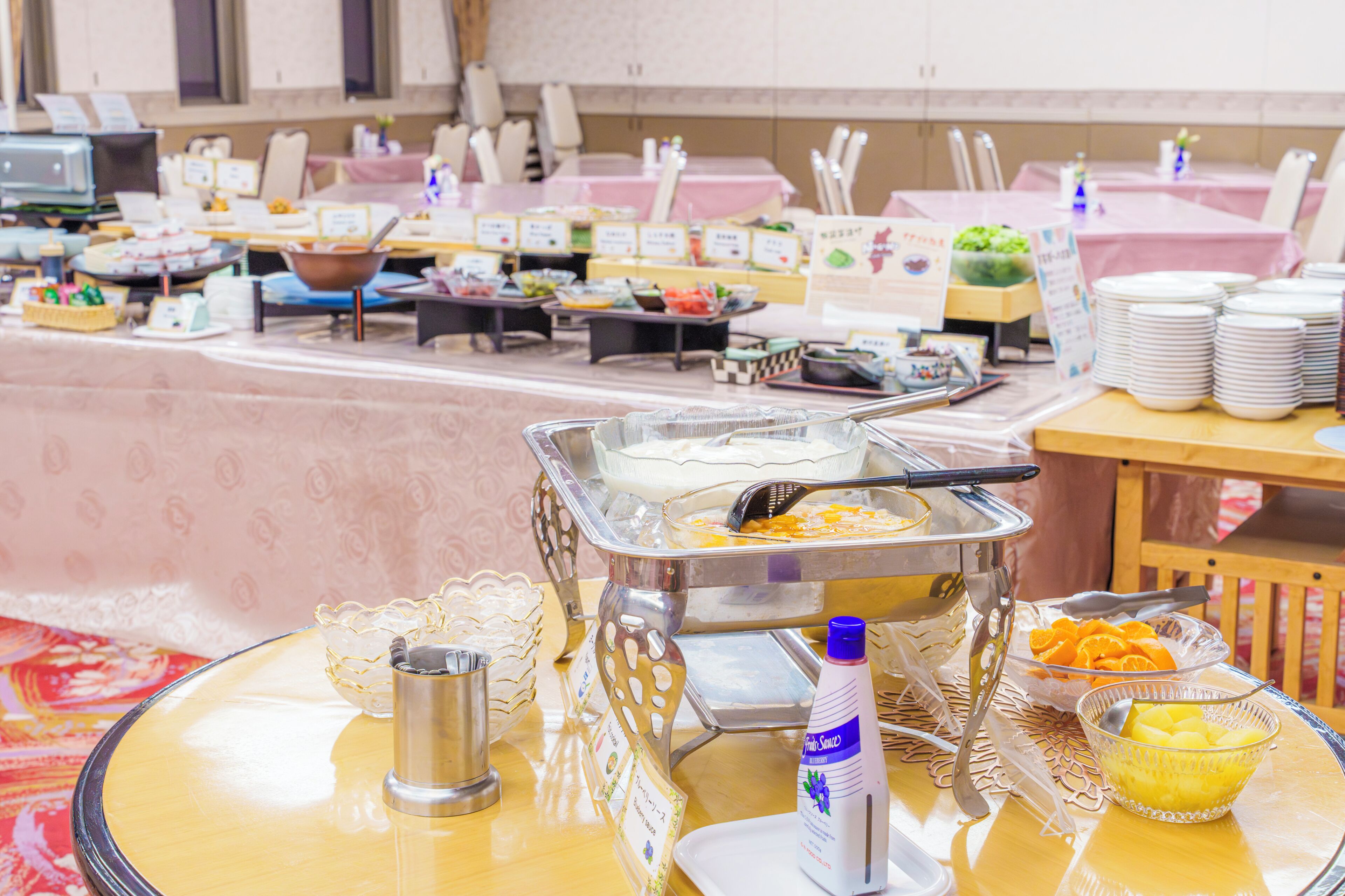 A buffet setup with various food items and utensils on tables, arranged in a spacious room with chairs and tables.