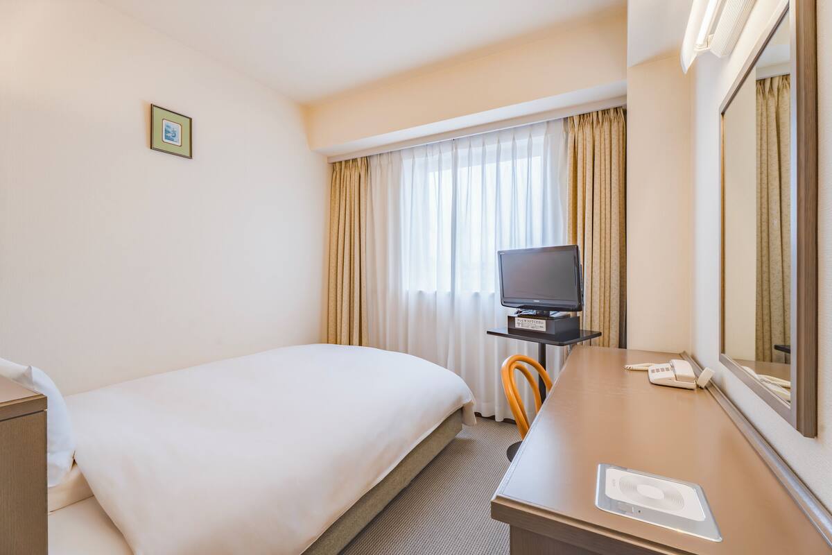 A hotel room with a bed, a desk with a television, a phone, and a mirror.