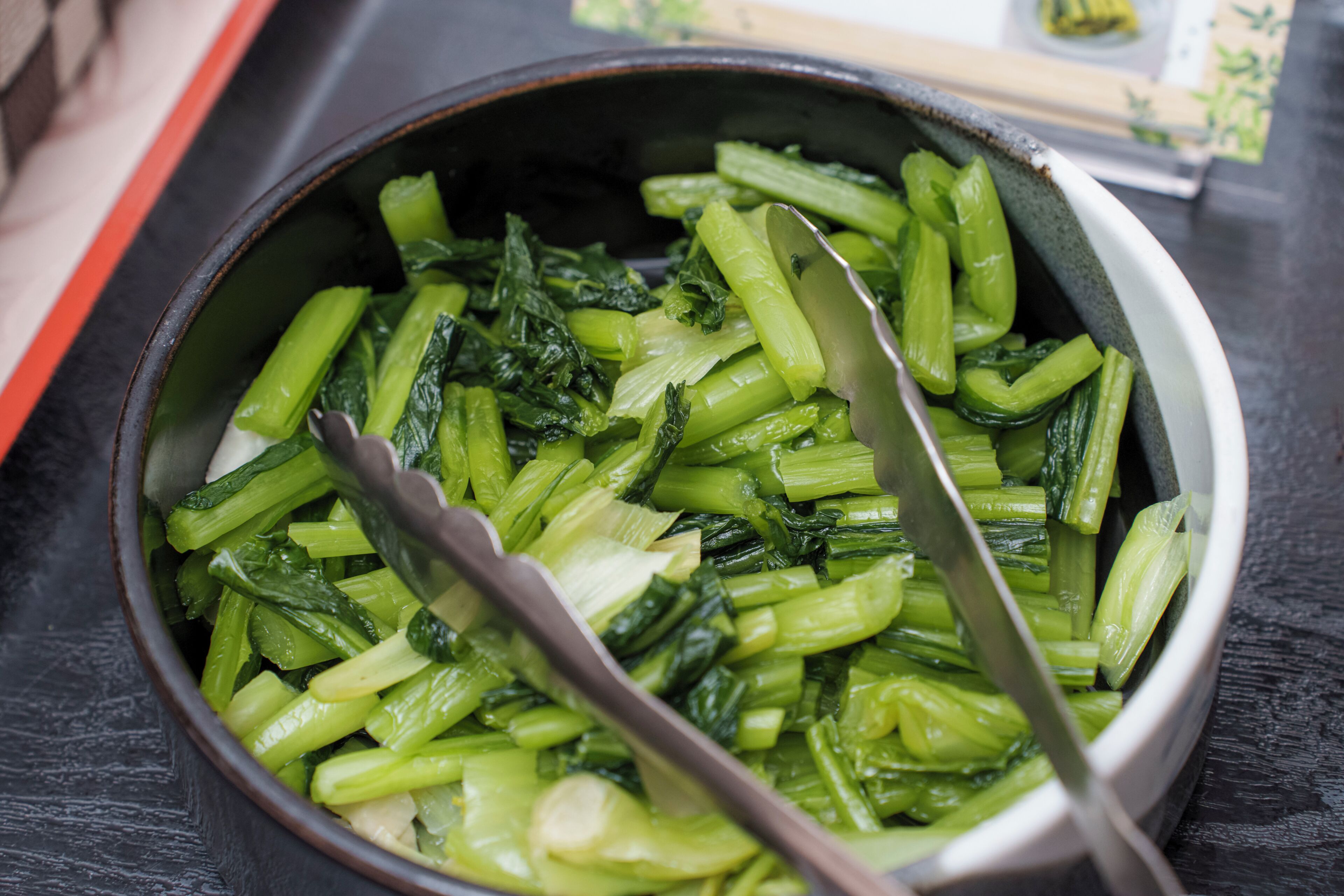 A bowl of cooked green vegetables with a spoon.