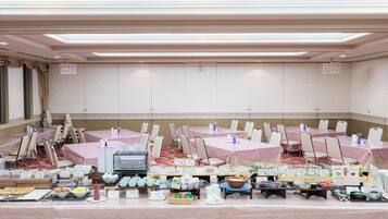 A banquet hall with tables covered in pink tablecloths, chairs, and a buffet setup with various food items.