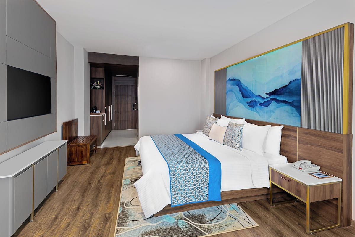 A modern hotel room with a large bed, bedside table, and a TV on the left.