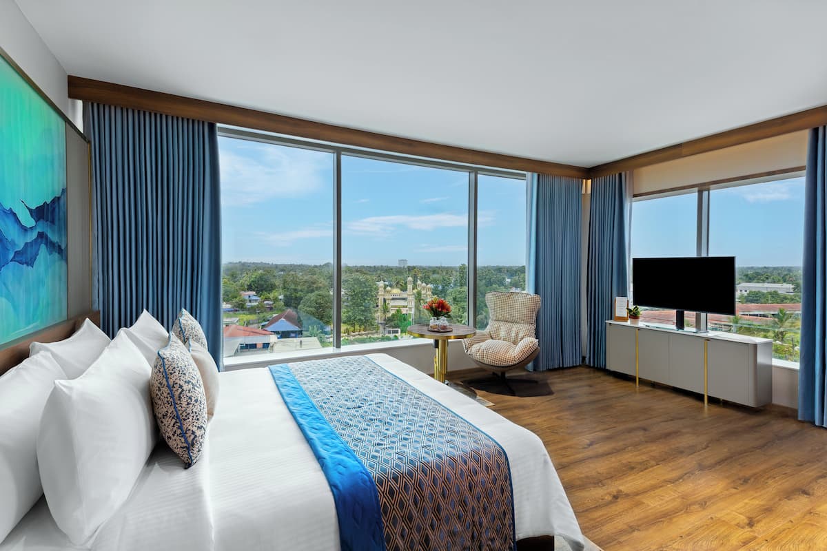 A hotel room with a large bed, a chair, a TV, and a view of the city.