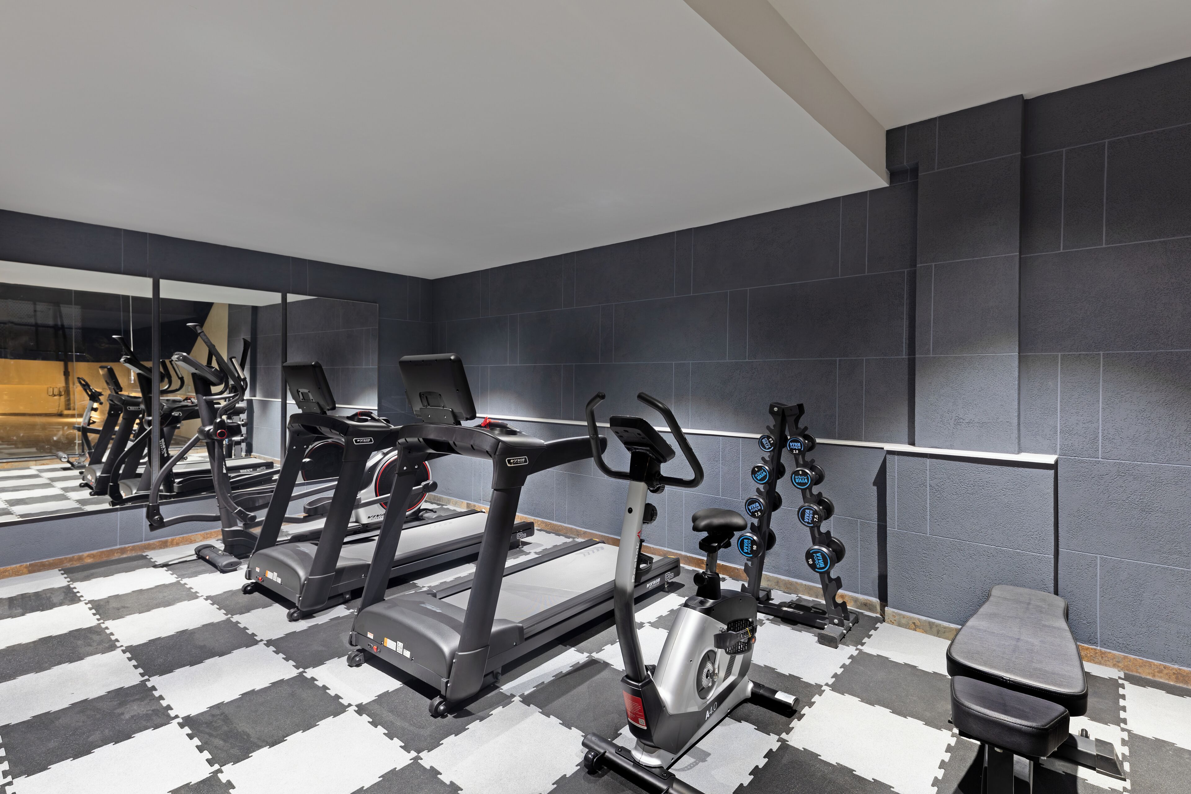 Une salle de sport équipée de matériel d’exercice, dotée d’un mur recouvert de miroirs et d’un sol à carreaux.