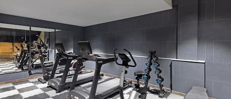 Un gimnasio con equipo de ejercicio, un espejo grande y suelo a cuadros.