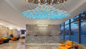 Un hall d’entrée moderne avec un comptoir de réception en marbre, des sièges orange et un grand élément décoratif au plafond.