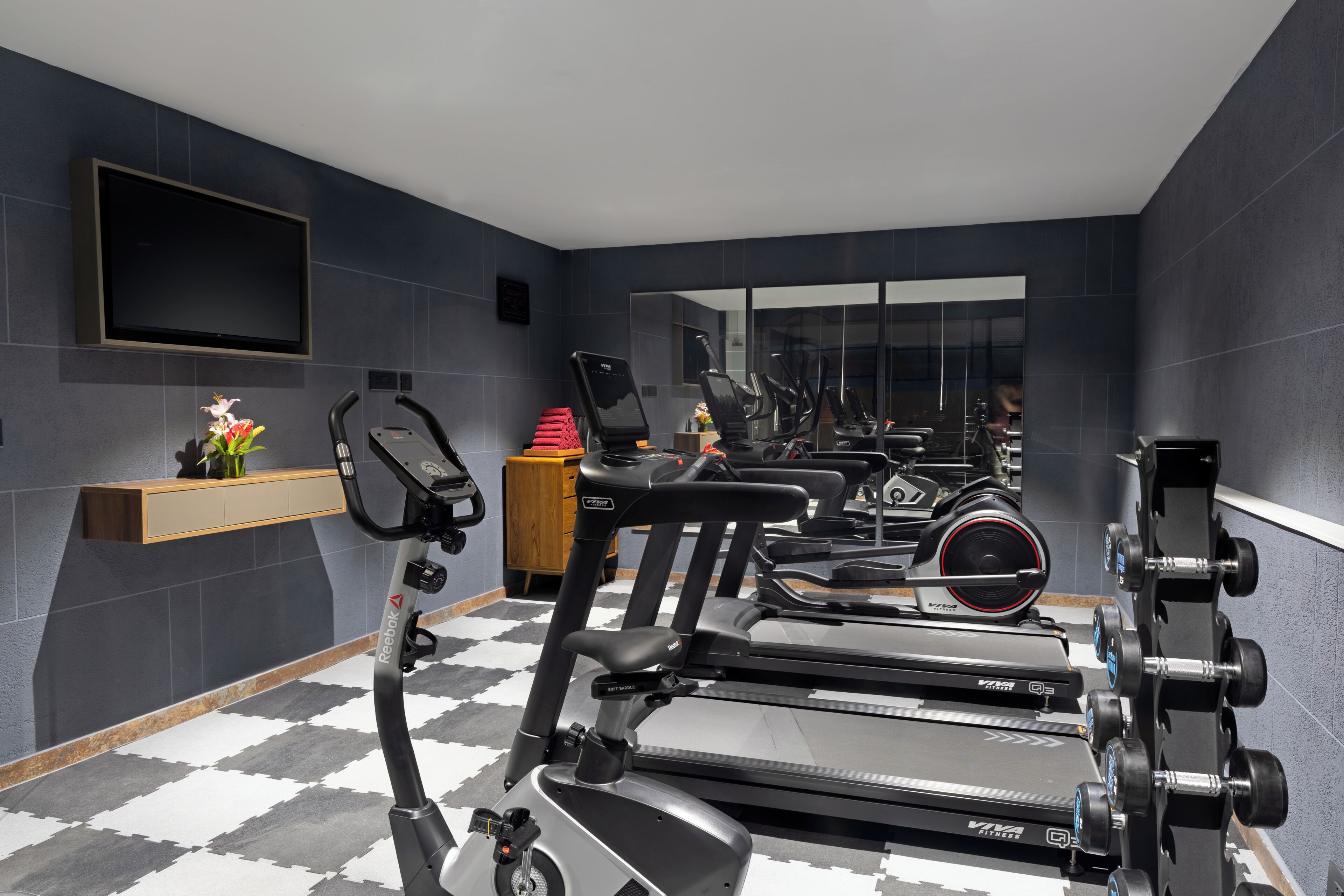 A modern gym with stationary bikes, treadmills, and dumbbells.