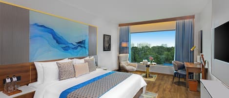 A hotel room with a large bed, a desk, a chair, a TV, and a window with a city view.