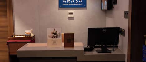 Een receptiebalie met een bord waarop 'AKASA' staat, een computermonitor, een televisie en een klein houten display.