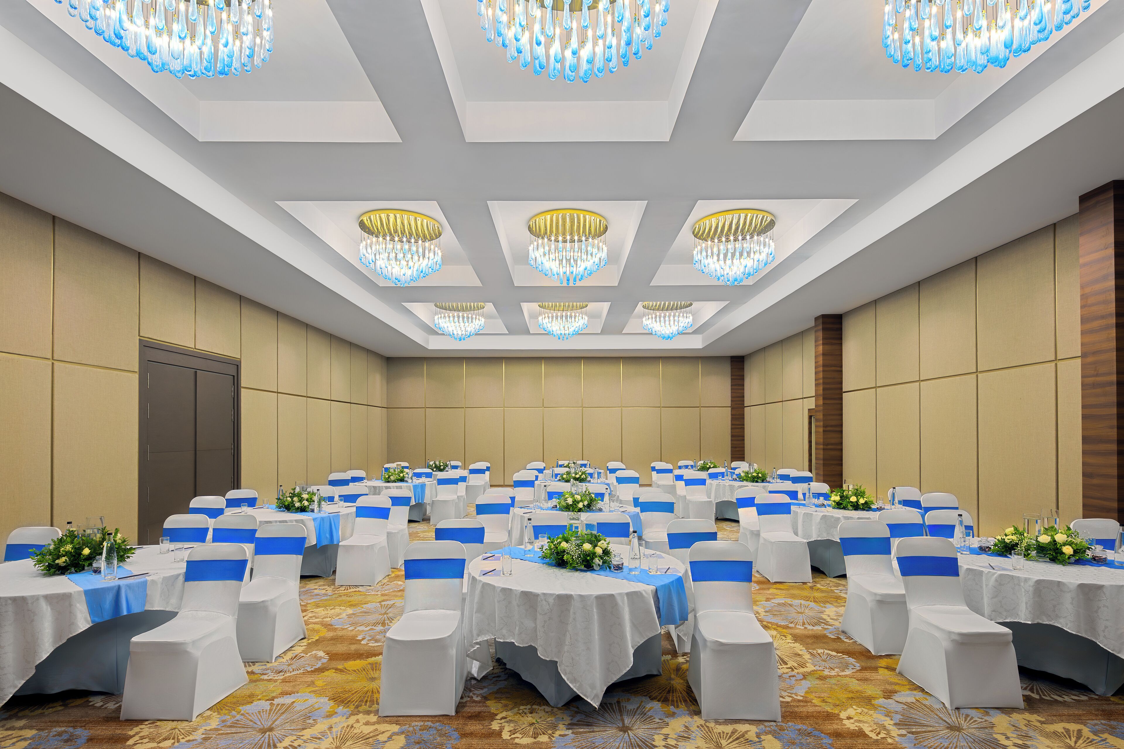 A conference room with round tables, white chairs, and blue sashes.