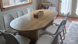 Un comedor con una mesa redonda, seis sillas, una lámpara y un ventanal con vista a árboles.