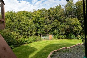 Un giardino curato con una struttura in legno, un prato verde e vegetazione rigogliosa.
