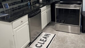 A modern kitchen with white cabinets, a black countertop, stainless steel appliances, and a 'CLEAN' doormat. - 2 Bdrm 2 Ba Gem, Where Comfort Meets Convenience
Sports, Fun, Eats & Campus Life (Arlington)