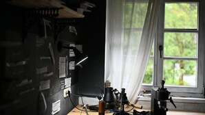 A room with a desk cluttered with papers, a lamp, and a coffee maker. A window with white curtains is visible, offering a view of greenery outside. - Peaceful Alpine Hideaway | Between Mountains & Streams (Bad Gastein)