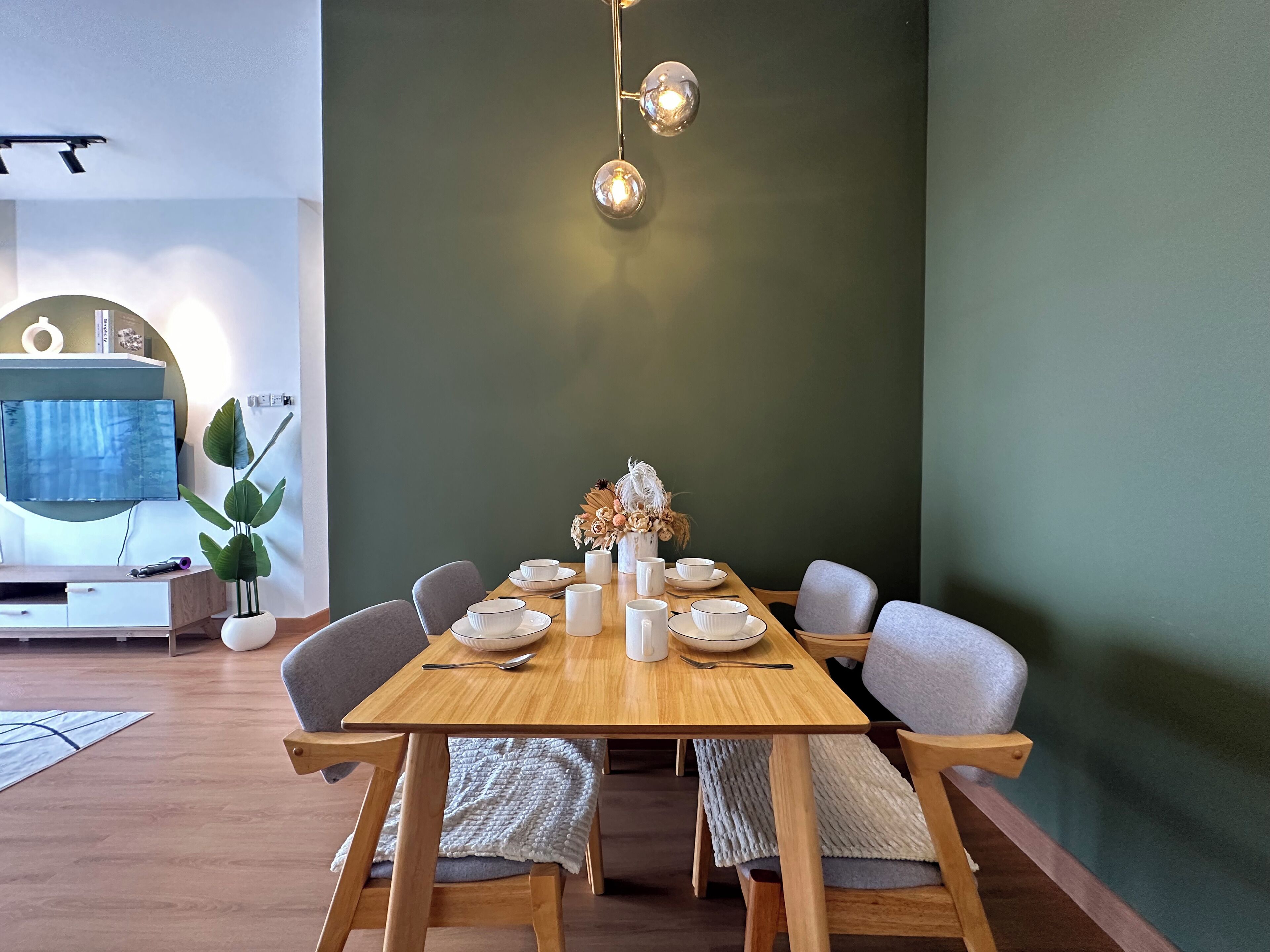Een eetgedeelte met een houten tafel voor vier personen, omringd door grijze stoelen, een vaas met gedroogde bloemen en een wandlamp.