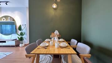 Een eetgedeelte met een houten tafel voor vier personen, omringd door grijze stoelen, een vaas met gedroogde bloemen en een wandlamp.