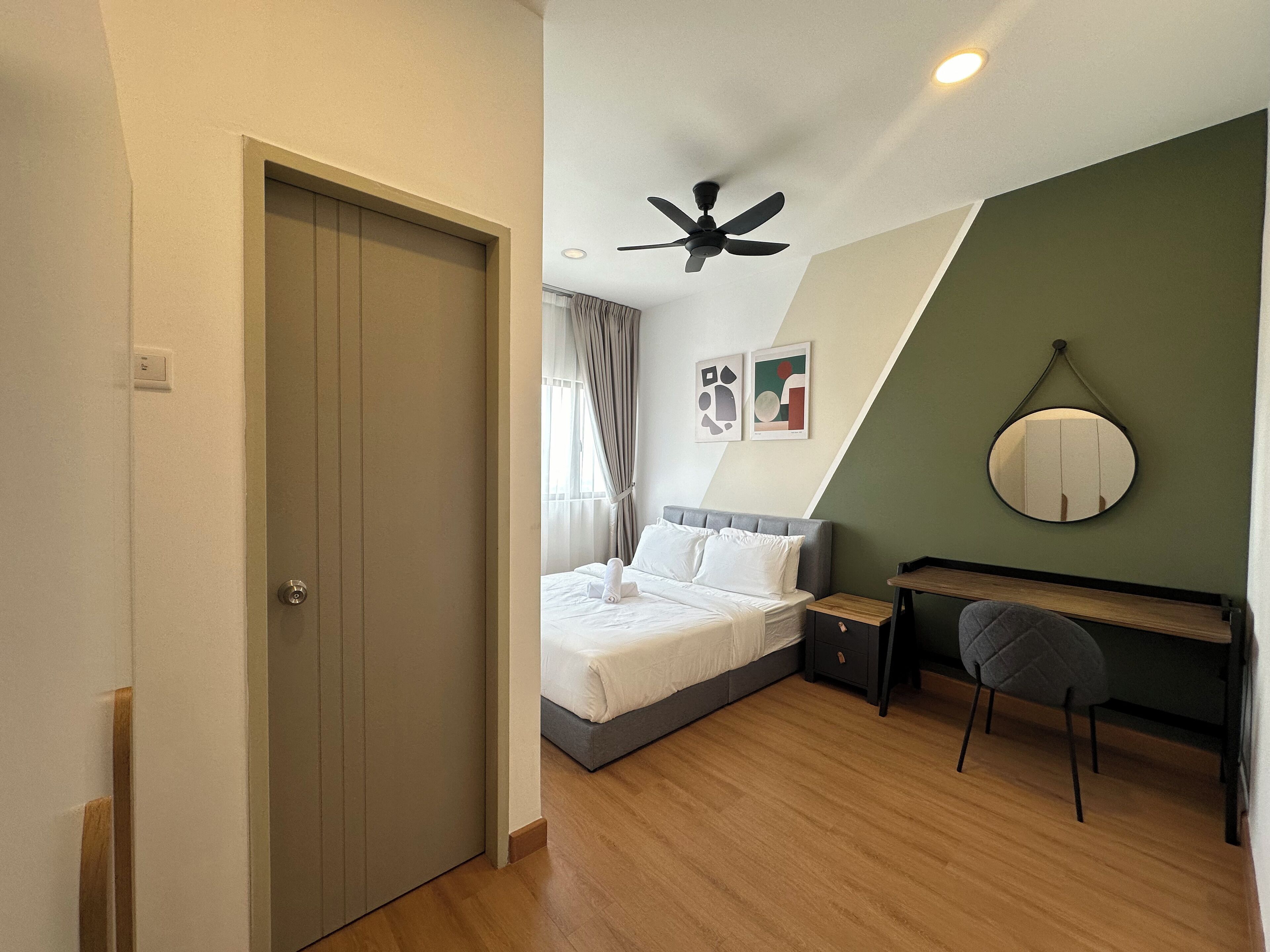 Une chambre à coucher comprenant un lit, un bureau, une chaise, un ventilateur de plafond et un miroir fixé au mur.