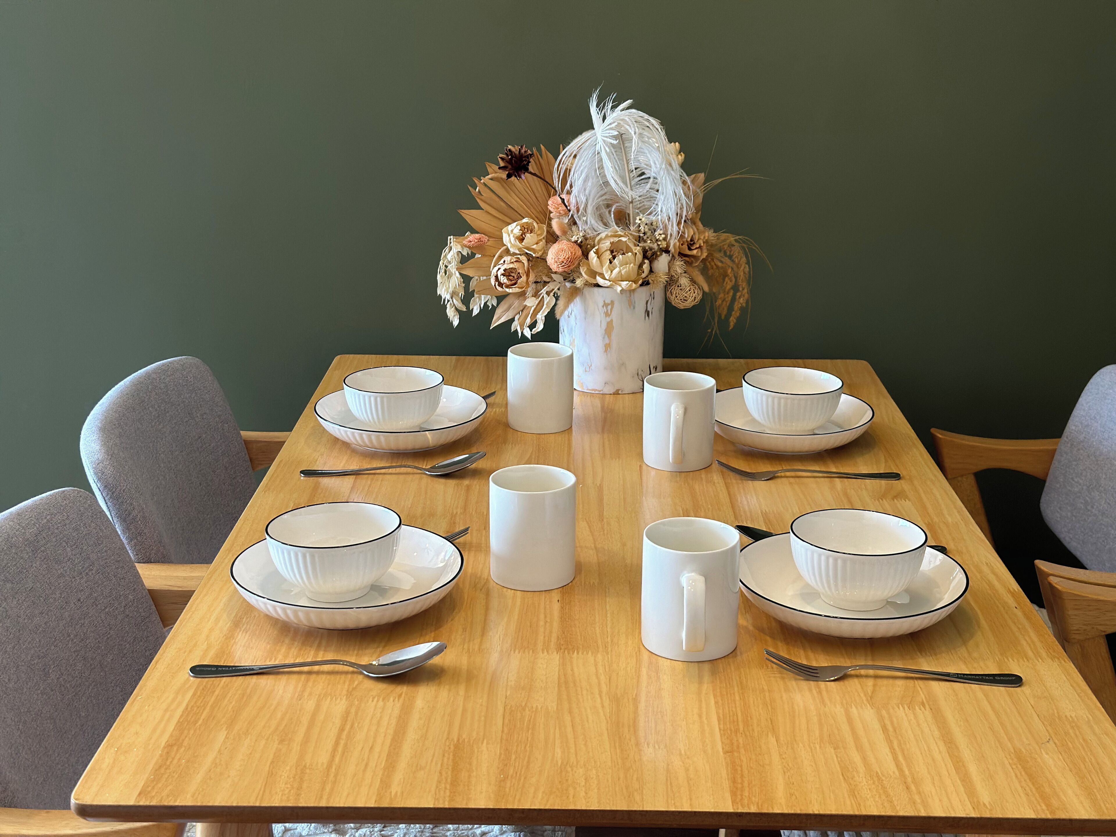 A dining table set with white bowls, plates, and cups, accompanied by silverware.