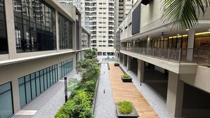 Un edificio moderno con un patio central, que cuenta con un pasillo de madera, plantas verdes y vistas a edificios altos al fondo.