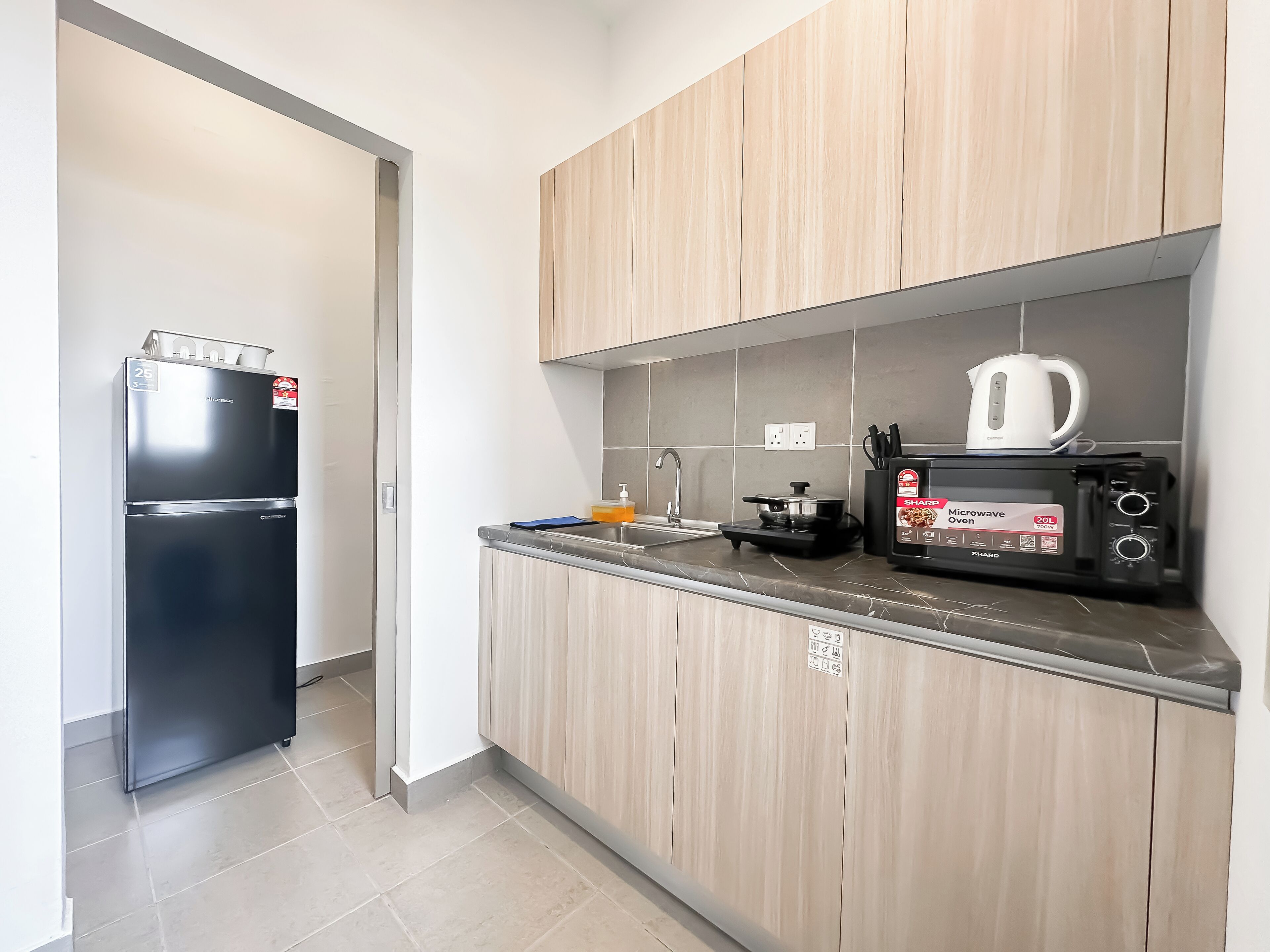 Una cocina moderna con un refrigerador, un horno microondas y una tetera sobre la encimera.