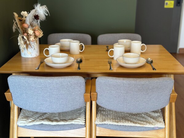 A dining table with white cups, saucers, and spoons, set for two.