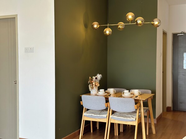 Un comedor con una mesa de madera dispuesta para cuatro, sillas grises tapizadas, un jarrón con flores secas y una lámpara de araña moderna.