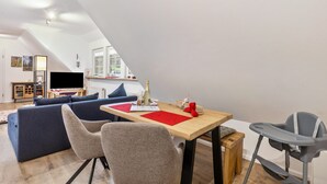 En moderne stue med spiseplads, sofa, stole, bord og en babystol.