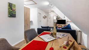 En moderne stue med spisebord, sofa og et fjernsyn i baggrunden.