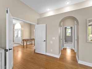 A spacious hallway with wooden flooring, white doors, and a visible bathroom with a shower and toilet.