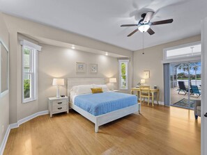 A bedroom with a bed, bedside tables, a desk, and a view of a patio with chairs.