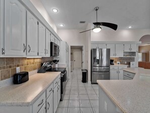A modern kitchen with white cabinets, a stainless steel refrigerator, a microwave, and a ceiling fan.