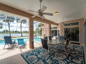 A covered outdoor area with a pool, lounge chairs, a table, and a ceiling fan.