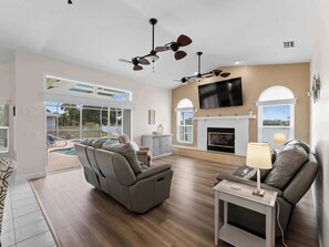A spacious living room with a fireplace, a large flat-screen TV, and a ceiling fan.