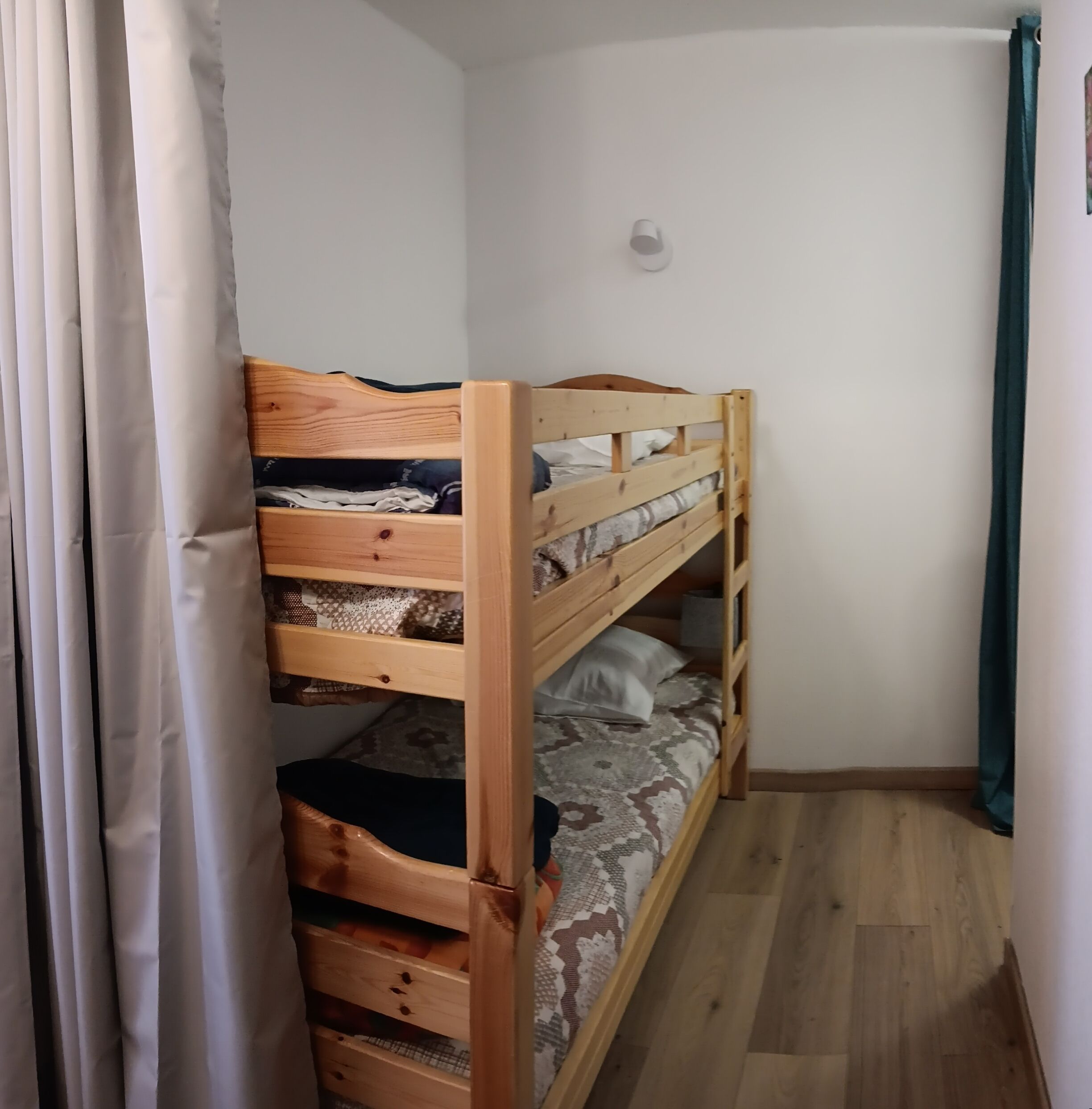 A bunk bed with a wooden frame, a small bedside table, and a patterned bedspread.